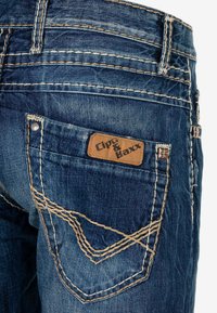 Denim spijkerbroek met een vervaagde, donkerblauwe wassing. Bevat zichtbare stiksels, een leren label met de tekst "Cipo & Baxx" en een gebogen ontwerp van de achterzakken.