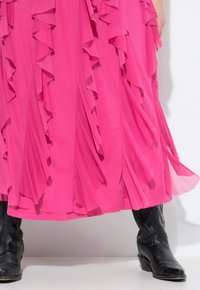 Vestido rosa de varias capas con volantes, hecho de tejido ligero, combinado con botas vaqueras negras de cuero con un detallado de costura.