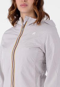 Giacca grigia chiara con cappuccio, zip frontale e dettagli a strisce multicolori. Presenta un tessuto texturizzato e un piccolo logo sul petto.