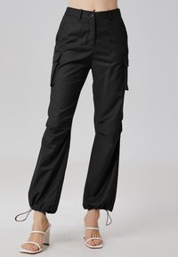Le pantalon cargo noir présente un design ajusté avec deux poches latérales, des poignets avec cordon de serrage et une fermeture à boutons à la taille. Adapté pour diverses occasions.