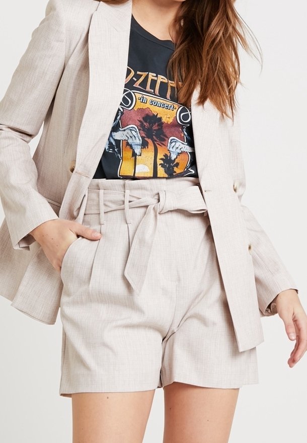 Femme portant un short beige clair ceinturé et un blazer assorti par-dessus un t-shirt noir à motif Led Zeppelin.