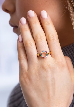 Guld ring med et åbent cirkeldesign, prydet med multikolorede ædelsten; glat overflade, minimalistisk stil og poleret tekstur.