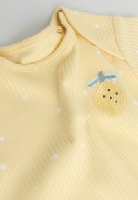 Rumena rebrasta otroška obleka z belimi pikami, okrašena z vezenim motivom ananasa z modrimi listi. Okrogel izrez in kratki rokavi.