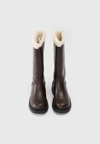 Bottes en cuir marron hautes jusqu'aux genoux, avec une doublure en fourrure crème douce en haut, dotées d'un bout rond et d'une semelle en caoutchouc noir texturé.