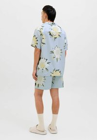 Blomster kortærmet skjorte og matchende shorts i lys blå stof. Har et stort cremet og grønt blomsterdesign. Glat tekstur og afslappet pasform.