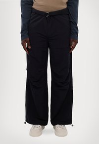 Pantaloni a gamba larga blu navy con cintura in tessuto e dettaglio a cerchio in metallo. Presentano aperture alla caviglia con zip e una texture liscia e leggera.