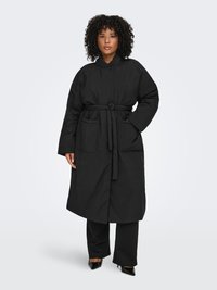 Svart skärpjacka med hög krage, långa ärmar, stora framfickor och quiltad textur. Bärs över svarta byxor och klackar.