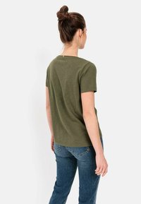 Olijfgroene, T-shirt met korte mouwen en een ronde halslijn met een subtiele textuur, in combinatie met blauwe jeans, gezien vanaf de achterkant.