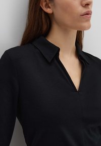 Chemise noire à col avec un design en V, fabriquée en tissu lisse. Dotée d'un col structuré et de détails de couture subtils.