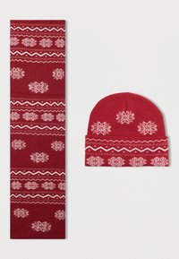 Conjunto de gorro e cachecol de malha vermelha com padrões de flocos de neve brancos, acentos em ziguezague e uma textura suave. Ambas as peças são projetadas para uso no inverno.