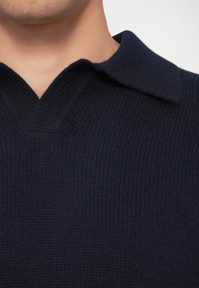 Marinblå stickad tröja med en texturerad yta, med V-hals och platt krage, som betonar värme och en klassisk stil.