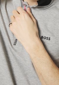 Gray polo shirt with a black collar and "BOSS" logo in black embroidery. Hand adjusting the collar, revealing subtle texture in the fabric.