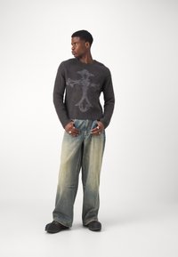 Gray knitted sweater with a cross design, paired with light blue wide-leg jeans and black footwear, featuring a relaxed fit and soft texture.