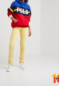 Sudadera con capucha roja y azul con el logo "POLO", combinada con pantalones ajustados amarillos y zapatillas blancas. Tejido suave y corte casual.