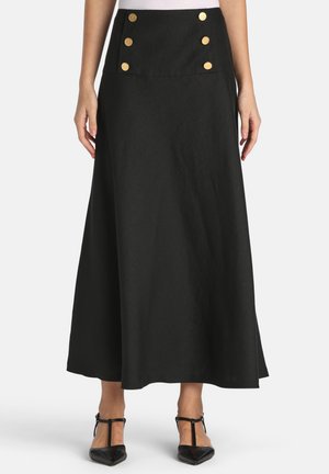 Žena nosí čiernu midi sukňu s vysokým pásom so šiestimi zlatými gombíkmi na prednej strane, v kombinácii s čiernymi lodičkami s T-priečkami.