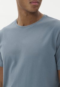 Tričko s krátkým rukávem ve světle modré barvě z bavlny. Má kulatý výstřih a hladkou strukturu s přiléhavým střihem. Žádné vzory ani akcenty nejsou viditelné.