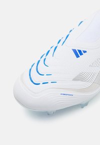 White soccer cleat with blue accent lines, textured surface, and silver detailing. Features prominently patterned upper and transparent studs.