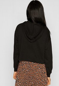 Felpa nera corta con cappuccio regolabile, abbinata a una gonna plissettata marrone con un motivo a leopardato bianco e nero.