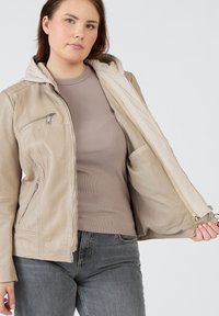 Beige läderjacka med avtagbar grå huva, dragkedja fram, sidorfickor och strukturerad yta, kombinerad med en ribbad beige topp.