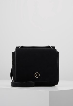 Sac bandoulière rectangulaire noir avec fermeture à rabat, logo circulaire argenté sur le devant, et sangle réglable reposant sur une surface blanche.