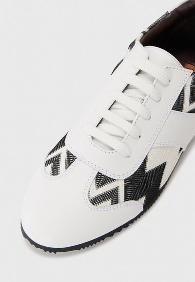 Λευκά αθλητικά παπούτσια με μαύρο και άσπρο γεωμετρικό σχέδιο. Διαθέτουν υφή από ύφασμα και δέρμα, στρογγυλή μύτη και επίπεδα κορδόνια. Ελαστική σόλα.