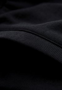 Gros plan sur un tissu noir avec une texture tissée visible et des plis, mettant en valeur le motif tricoté et les détails du matériau doux.