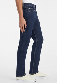 Vaqueros de denim azul marino con un corte recto, que presentan detalles de costura, diseño de cinco bolsillos y cierre de cremallera.