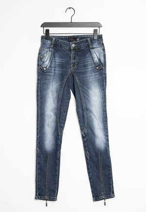 Blå denimjeans med falmet vask, knap- og lynlåslukning, skrå forlommer med trykknapper, lynlåsdetailler ved ankellommer.