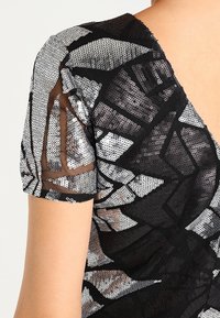 Svart topp med åtsittande design som har geometriska silverpaljetter. Korta ärmar och genomskinlig textur förstärker det visuella detaljerna.