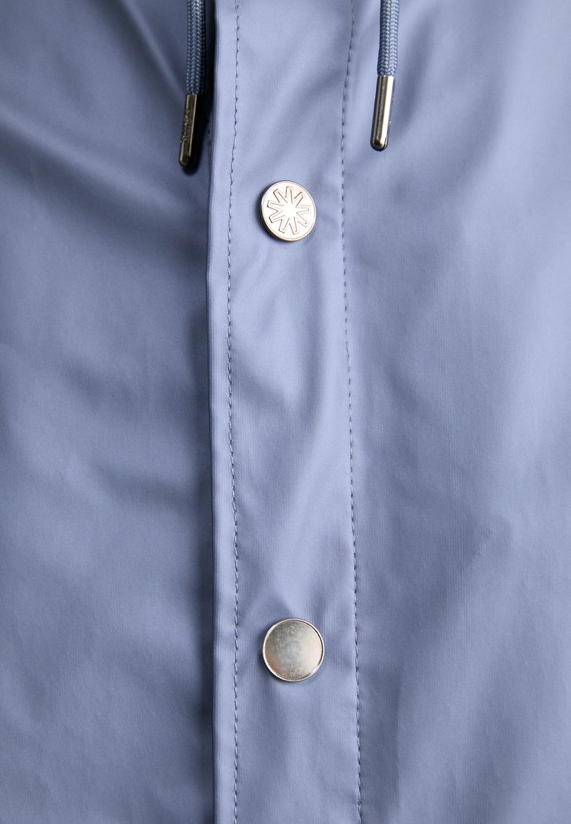 Light blue jacket close-up featuring a silver snap button and blue drawstrings, with smooth texture and fine stitching details.