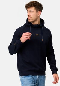 Marineblå hættetrøje med snøre, prydet med et gult broderet logo på brystet. Lavet af et blødt stof med ribbede manchetter og kant.