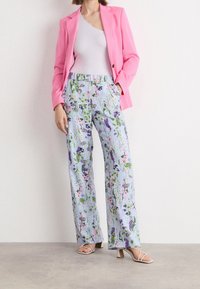 Lichtblauwe bloemenbroek met een losse pasvorm en elastische tailleband, gecombineerd met een roze blazer en een grijze tanktop. Open tenen beige hakken.