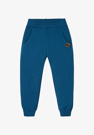 Niebieska koszulka z wzorem, z krótkim rękawem i kieszenią na piersi, zestawiona z ciemnoniebieskimi zwężanymi spodniami oraz jasnymi butami wsuwanymi.