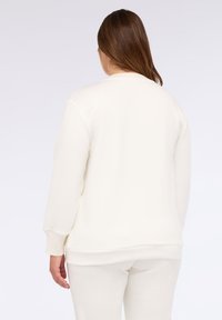 Felpa color crema con maniche lunghe, scollatura rotonda, e polsini e orlo a coste. Tessuto morbido al tatto, design minimalista.