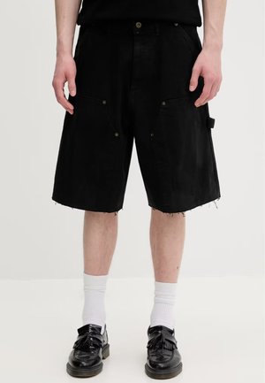 Modèle portant un short cargo noir longueur genou à l’ourlet brut, des chaussettes blanches montantes et des mocassins noirs à pampilles.
