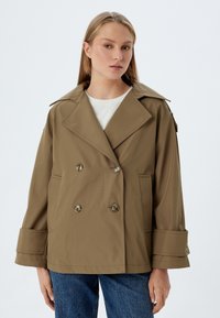 Chaqueta marrón de doble botonadura con solapas anchas, un ajuste relajado y grandes botones. Cuenta con bolsillos laterales y mangas hasta los codos.