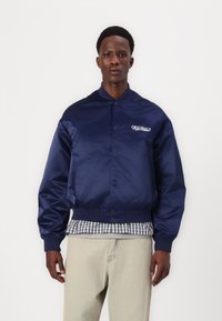 Chaqueta de bombardero navy hecha de tela brillante con cierre de botones y puños acanalados. Presenta el logo "ORIGINALS" en el lado izquierdo del pecho.