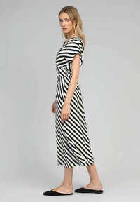 Robe maxi rayée noir et blanc avec un décolleté en V, des manches courtes et une taille ajustée. Texture lisse, longueur cheville, associée à des ballerines noires.