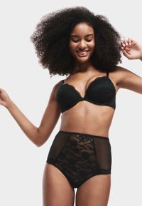 Schwarzes Spitzen-Bralette mit Unterdraht und gewellten Kanten, kombiniert mit hochgeschnittenen schwarzen Spitzenpanties, die über florale Muster und Netzpaneele verfügen.