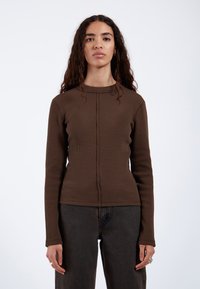 Brown, long-sleeve top with a ribbed texture, round neckline, and central seam detail. Paired with dark jeans.