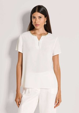 Witte blouse met korte mouwen, V-hals en gouden bies. Glad stof, losse pasvorm en subtiele naaddetails. Gecombineerd met lichtgekleurde broek.