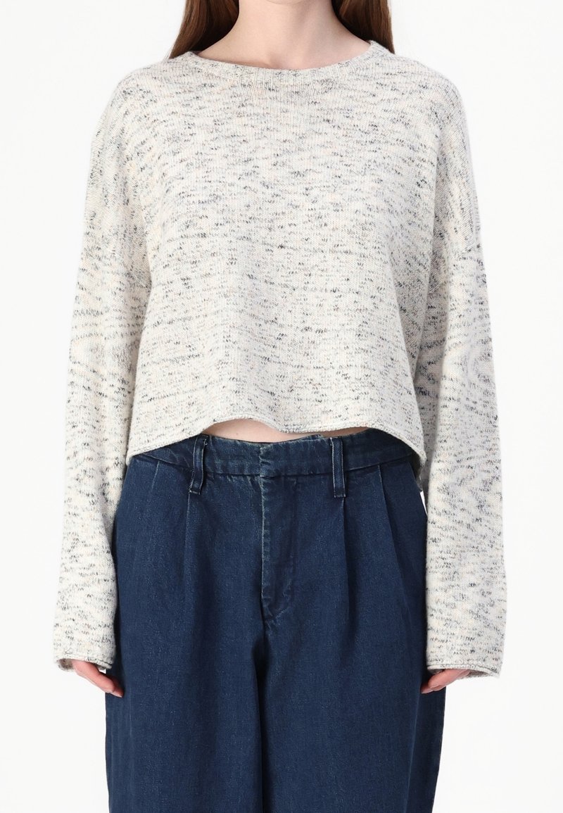 Jasnoszary sweter z fakturą, o okrągłym dekolcie, krótkim fasonie i długich rękawach, zestawiony z wysokowarstwowymi ciemnymi jeansami.
