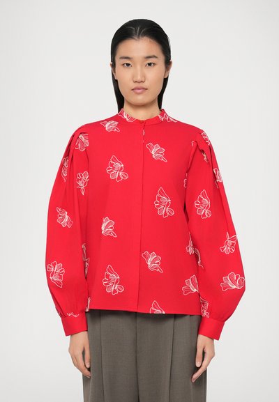Rote Bluse mit weißer floraler Stickerei, hohem Ausschnitt und Ballonärmel, aus leichtem Stoff mit glatter Textur.