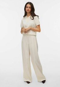 Kremowa koszulka polo z krótkim rękawem i plisą na guziki, w zestawieniu z beżowymi, szerokimi spodniami o wysokim stanem. Gładka tkanina i dopasowany krój.