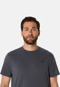 Grå kortærmet t-shirt i blødt stof, med rund hals og et lille mørkegrønt logo på venstre brystområde.