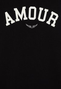 Černé tričko s výrazným bílým nápisem "AMOUR" a vyšitým detailem křídla pod nápisem. Měkká bavlněná tkanina s hladkou strukturou.