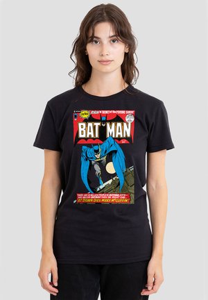 Young woman with long hair wearing black Batman comic cover t-shirt featuring Batman leaping over rooftops at night.