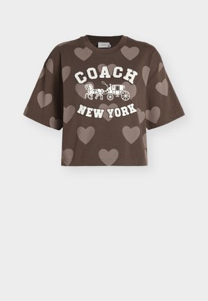 Καφέ κοντό t-shirt με ανοιχτόχρωμα σχέδια καρδιών, λευκό κείμενο "COACH", γραφικό άμαξας με άλογο και κείμενο "NEW YORK" μπροστά.