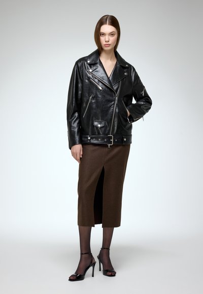 Black leather motorcycle jacket with zippered pockets, paired with a brown knee-length skirt featuring a front slit and black high-heeled sandals.