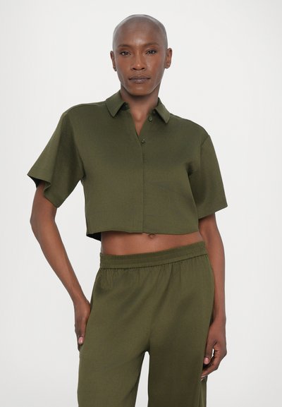 Chemise à manches courtes, courte, à boutons en tissu vert foncé, associée à un pantalon décontracté assorti avec une taille élastique.